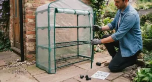 A person assembling a 4-tier mini greenhouse in a back garden, demonstrating the simple tool-free build.